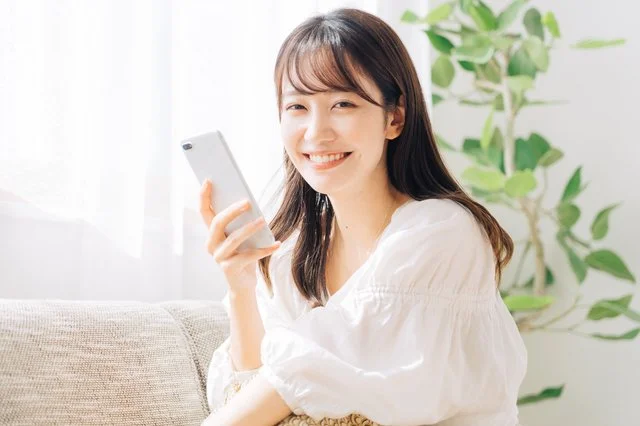 ソファでスマートフォンを手に微笑む女性